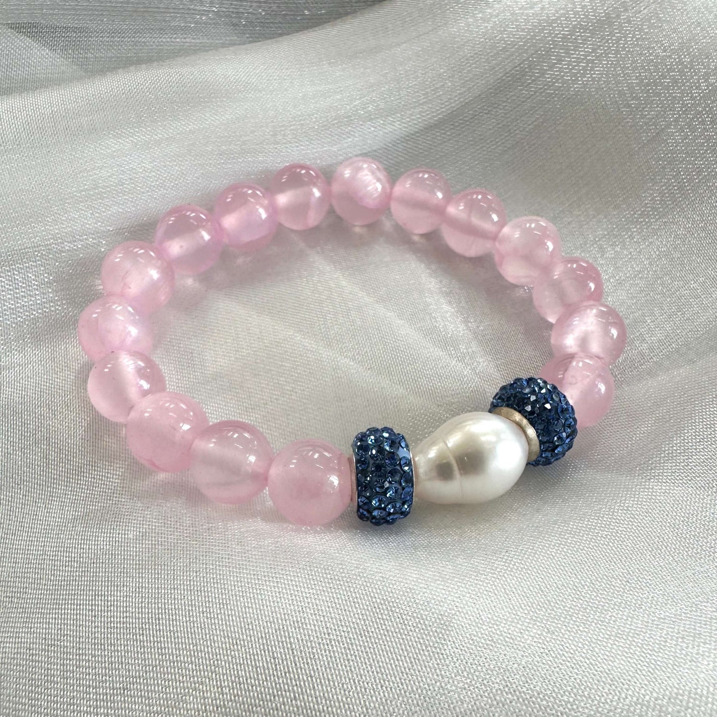 Pink jade bracelet featuring 10mm jade beads, freshwater pearl, and rhinestone accents on a soft fabric background.