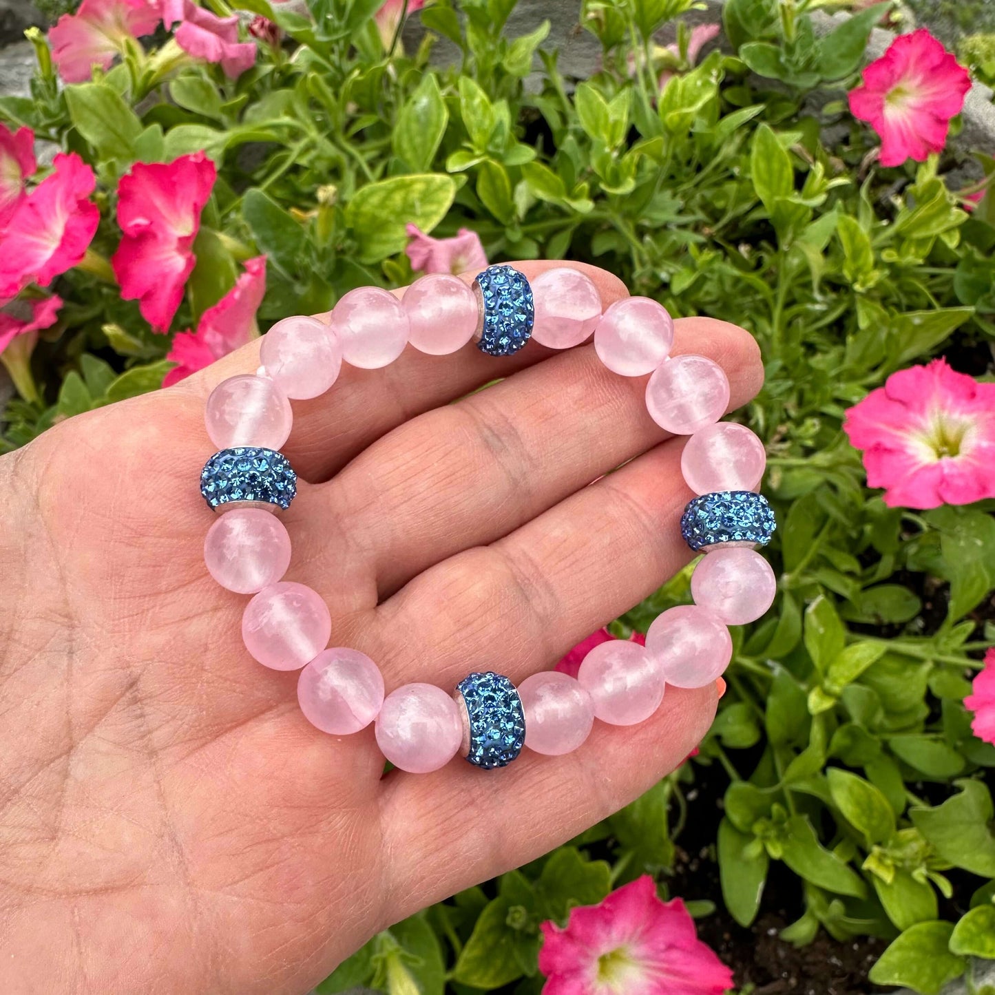 Pink jade bracelet featuring 10mm pink jade beads, freshwater pearl, and blue rhinestone accents, displayed in a hand.