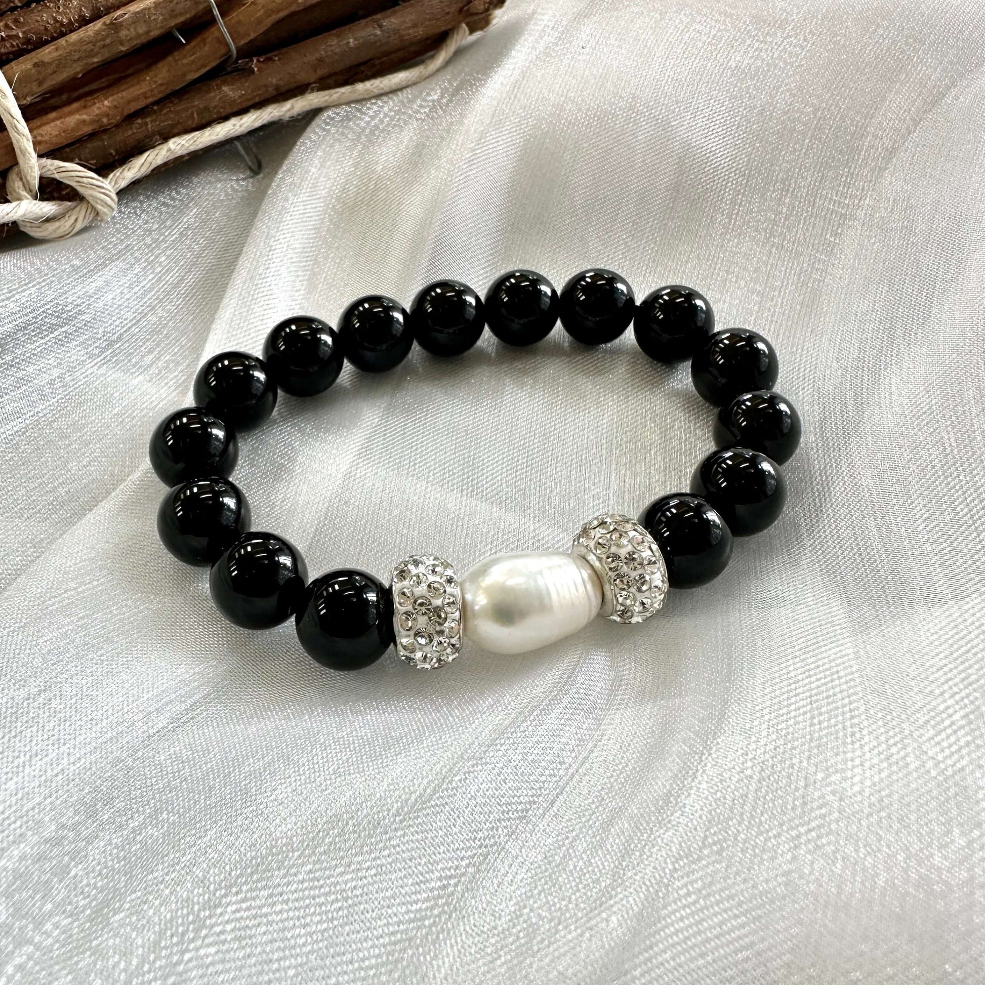 Close-up of black onyx bracelet with pearl shown on white cloth