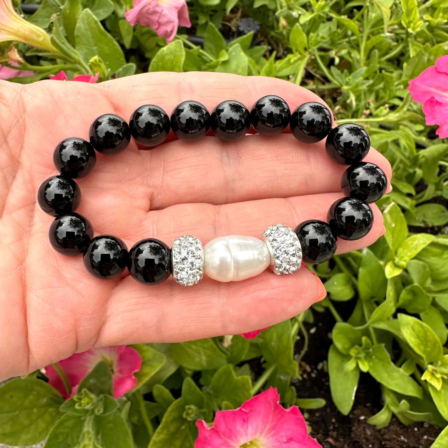 Black onyx bracelet with pearl held in hand against green foliage