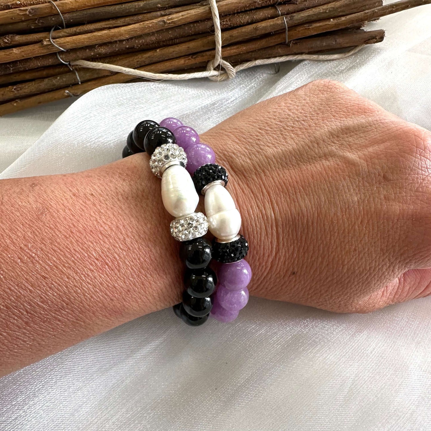Two black onyx bracelets with pearls worn on a model’s wrist