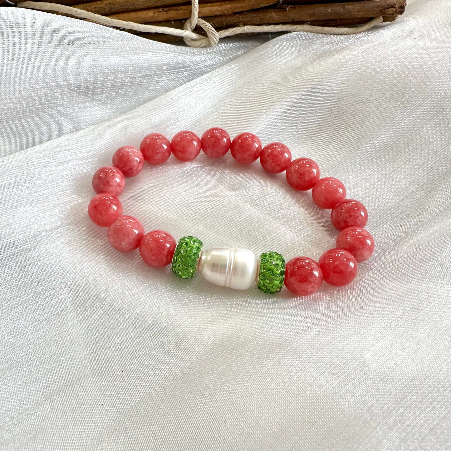 Red jade bracelet with pearl and green rhinestones displayed on white cloth