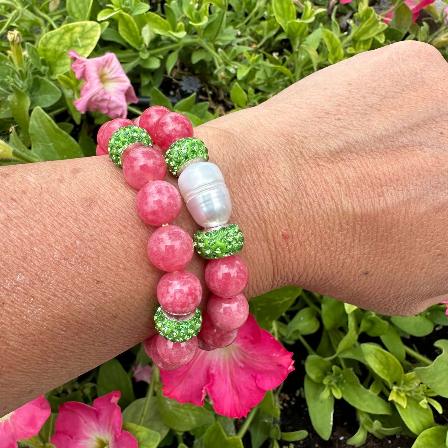 Two red jade bracelets with green rhinestones, one with a pearl, worn on a woman’s wrist