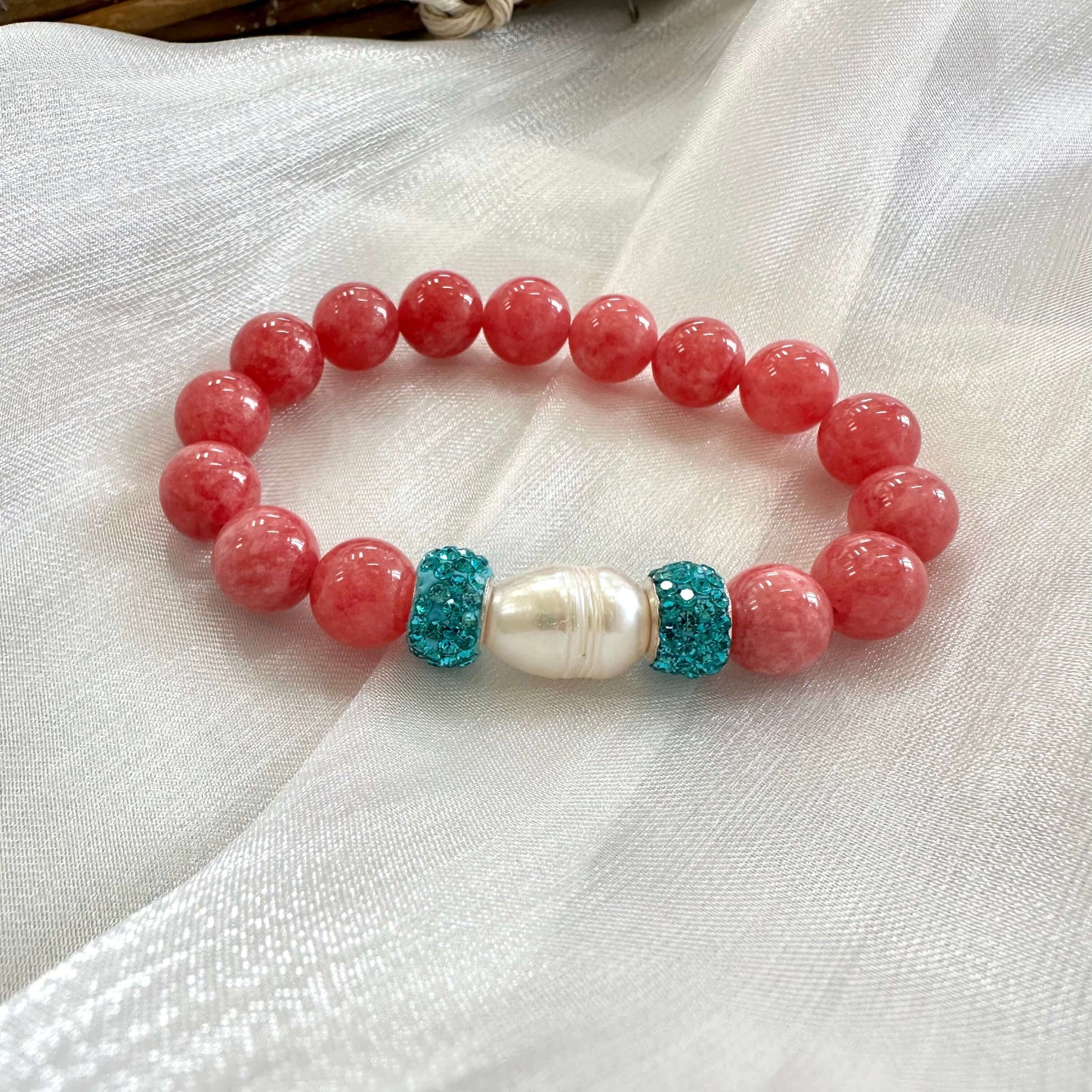 Red jade bracelet with pearl and blue rhinestones displayed on white cloth