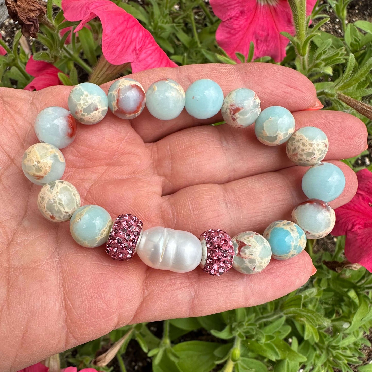 Blue opal jasper bracelet held in hand against green foliage