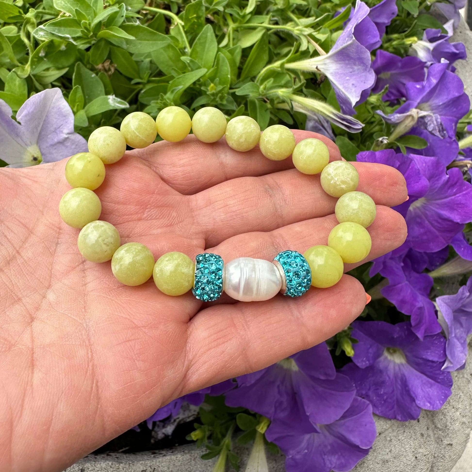 Olive green jade bracelet with one pearl held in hand near purple flowers