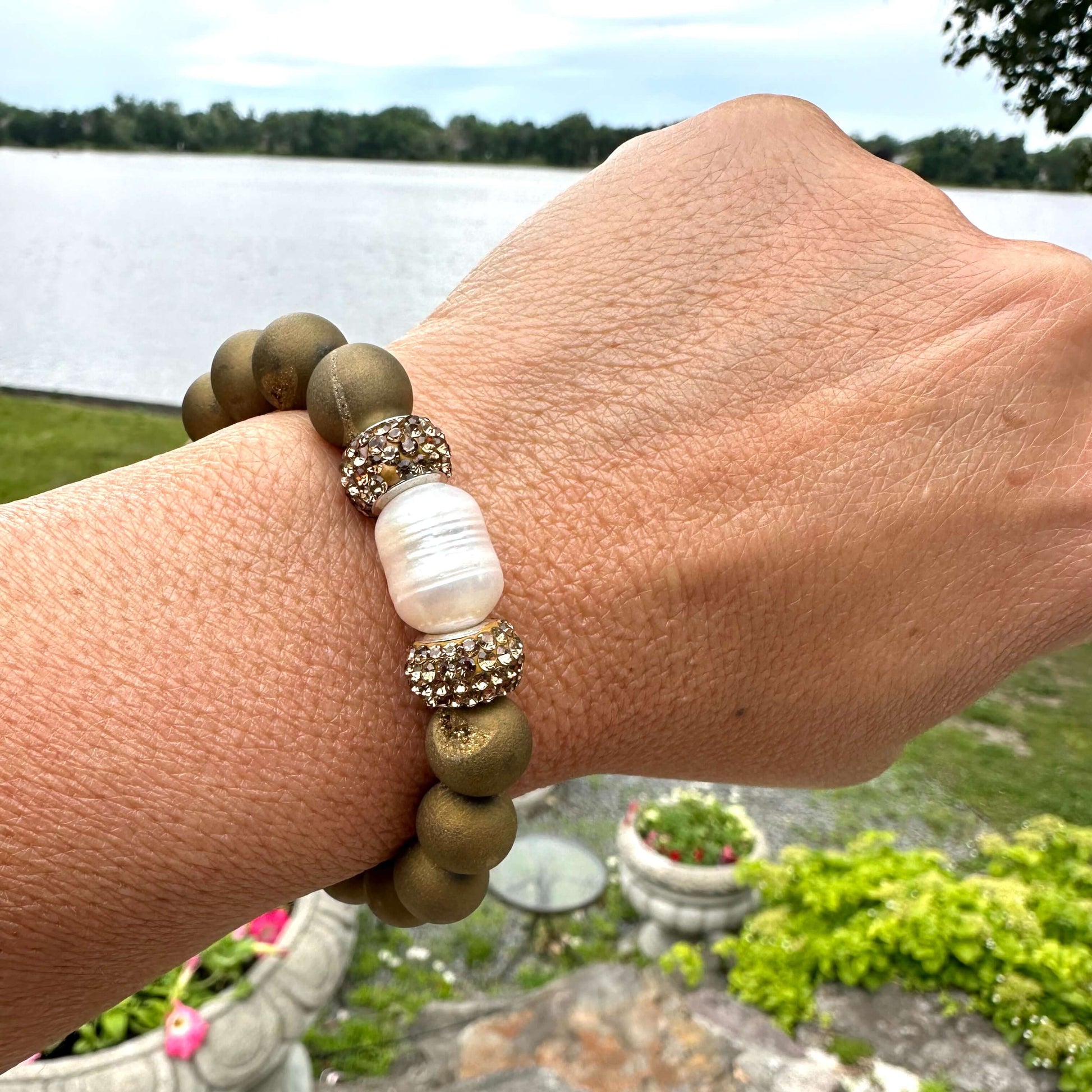 Gold druzy agate bracelet with pearl worn on a woman’s wrist outdoors