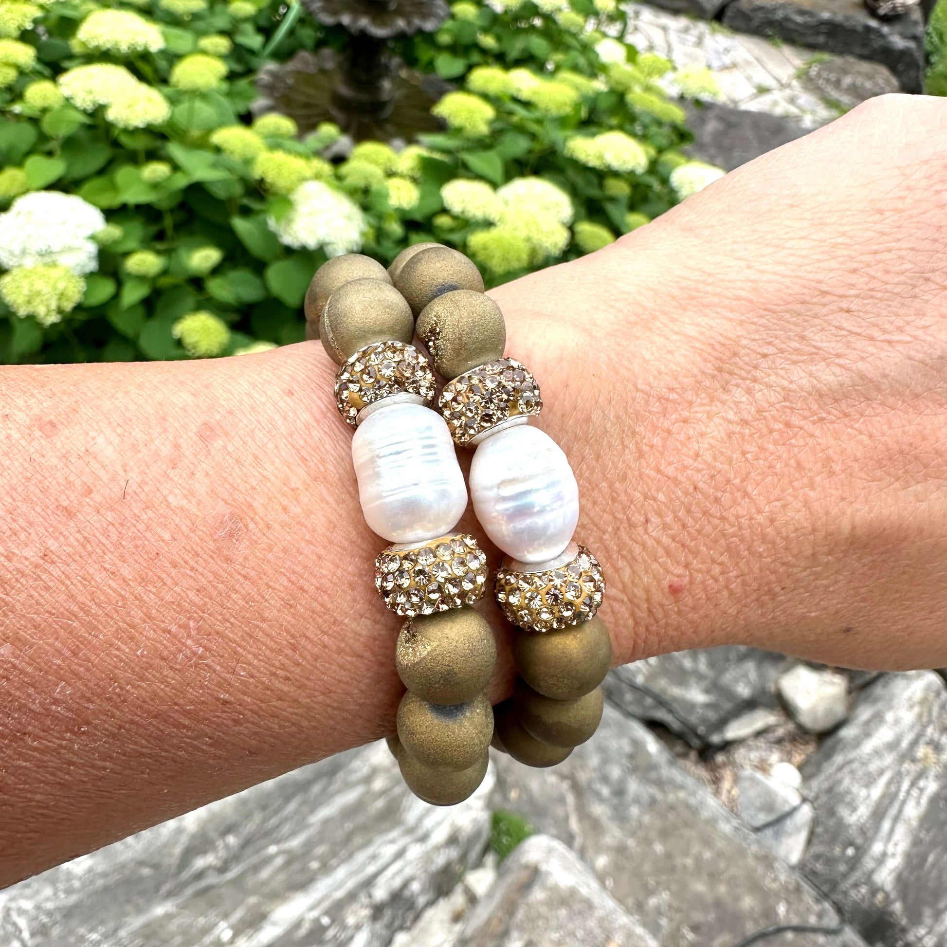 Two gold druzy agate bracelets stacked on a woman’s wrist in summer light