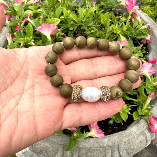 Hand holding gold druzy agate bracelet with pearl near a lakeside