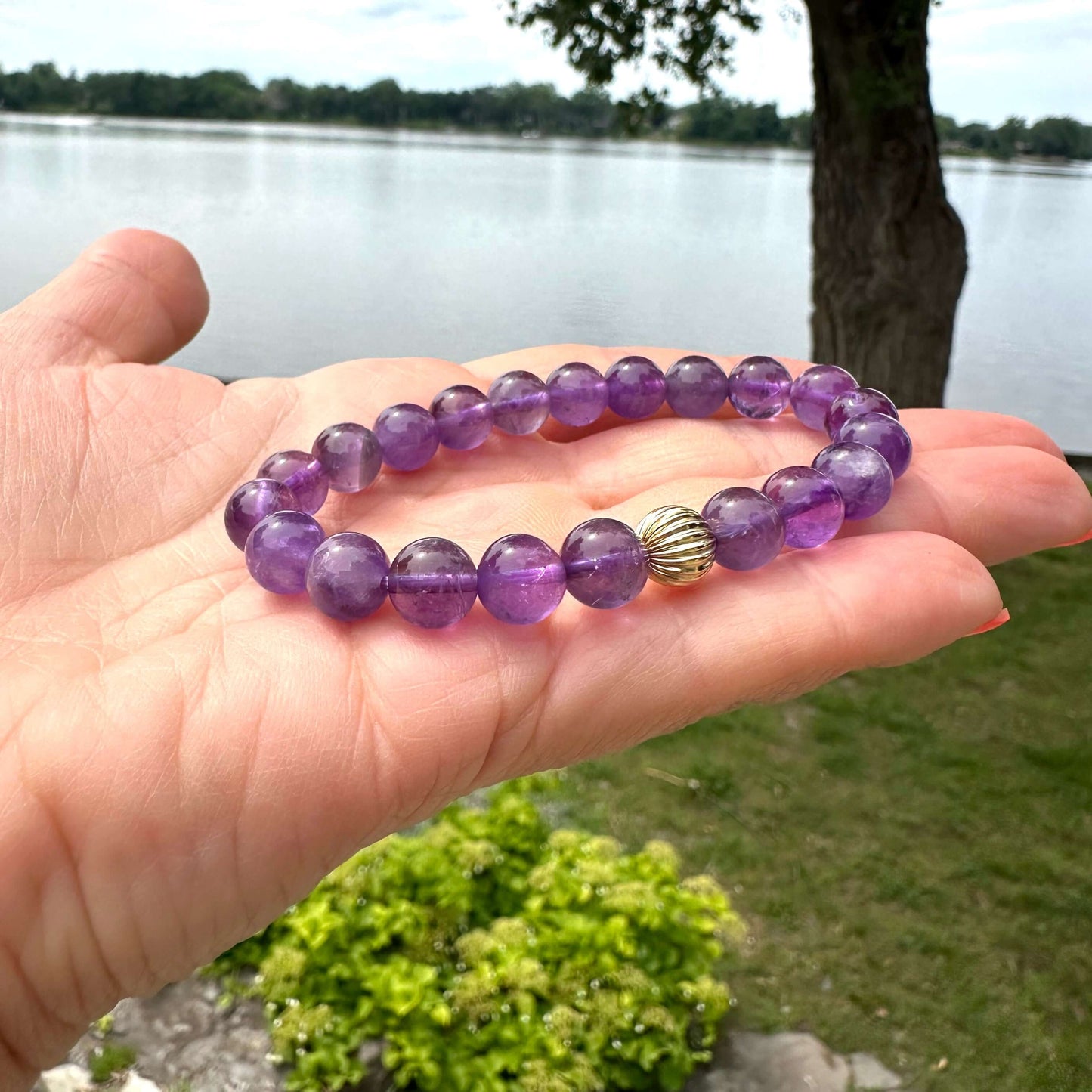 Amethyst bracelet close up held in hand outdoors by water and trees