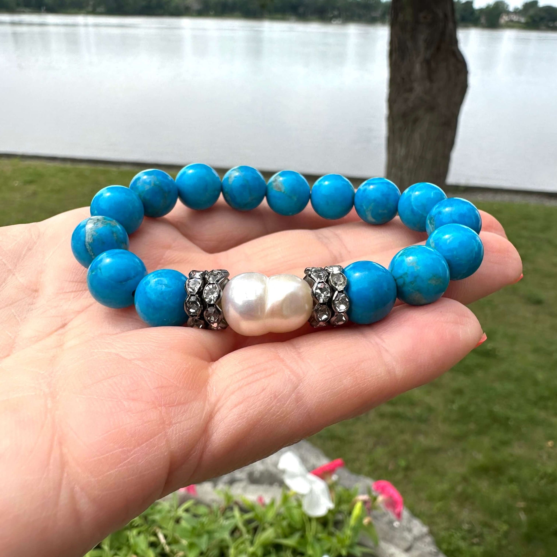 Turquoise howlite pearl bracelet held in hand against natural foliage