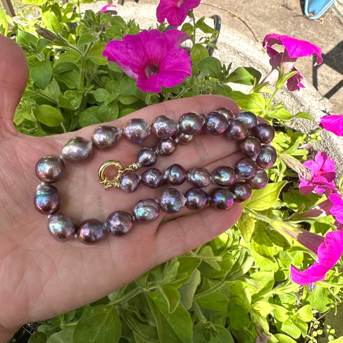 Purple Edison baroque pearl necklace held in hand against natural foliage