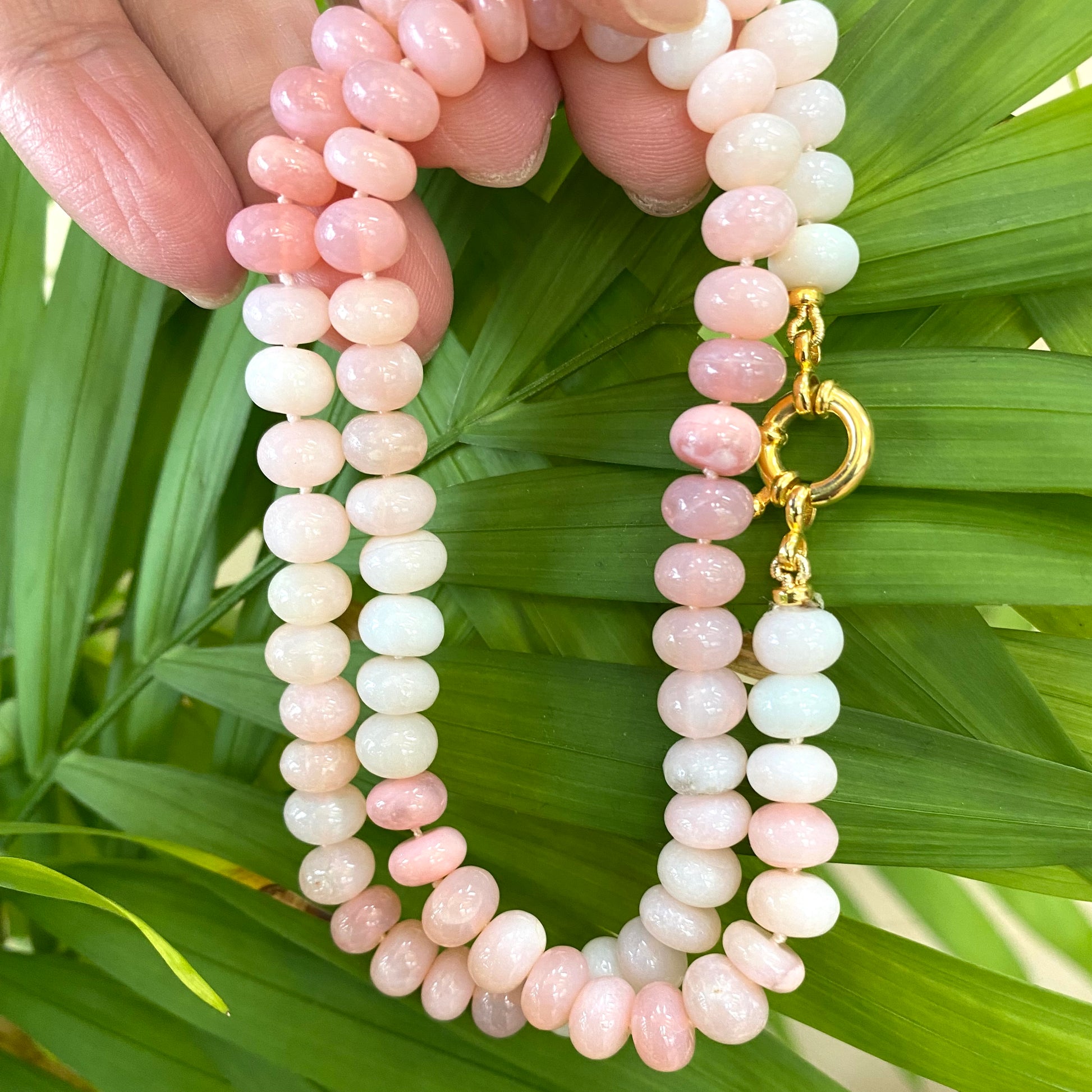 Pink opal beaded necklace close-up in hand with natural foliage