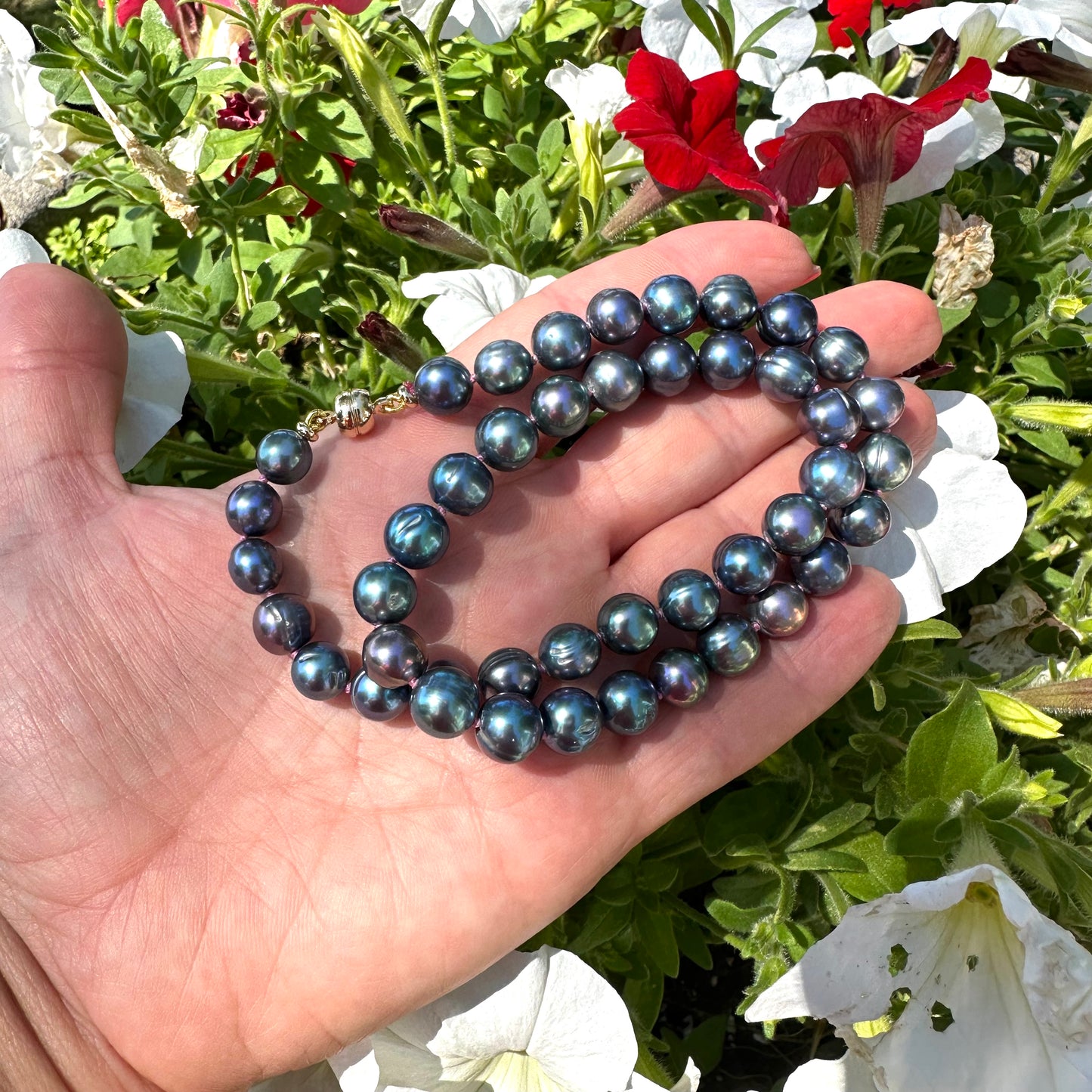 Peacock pearl necklace held in hand against green foliage