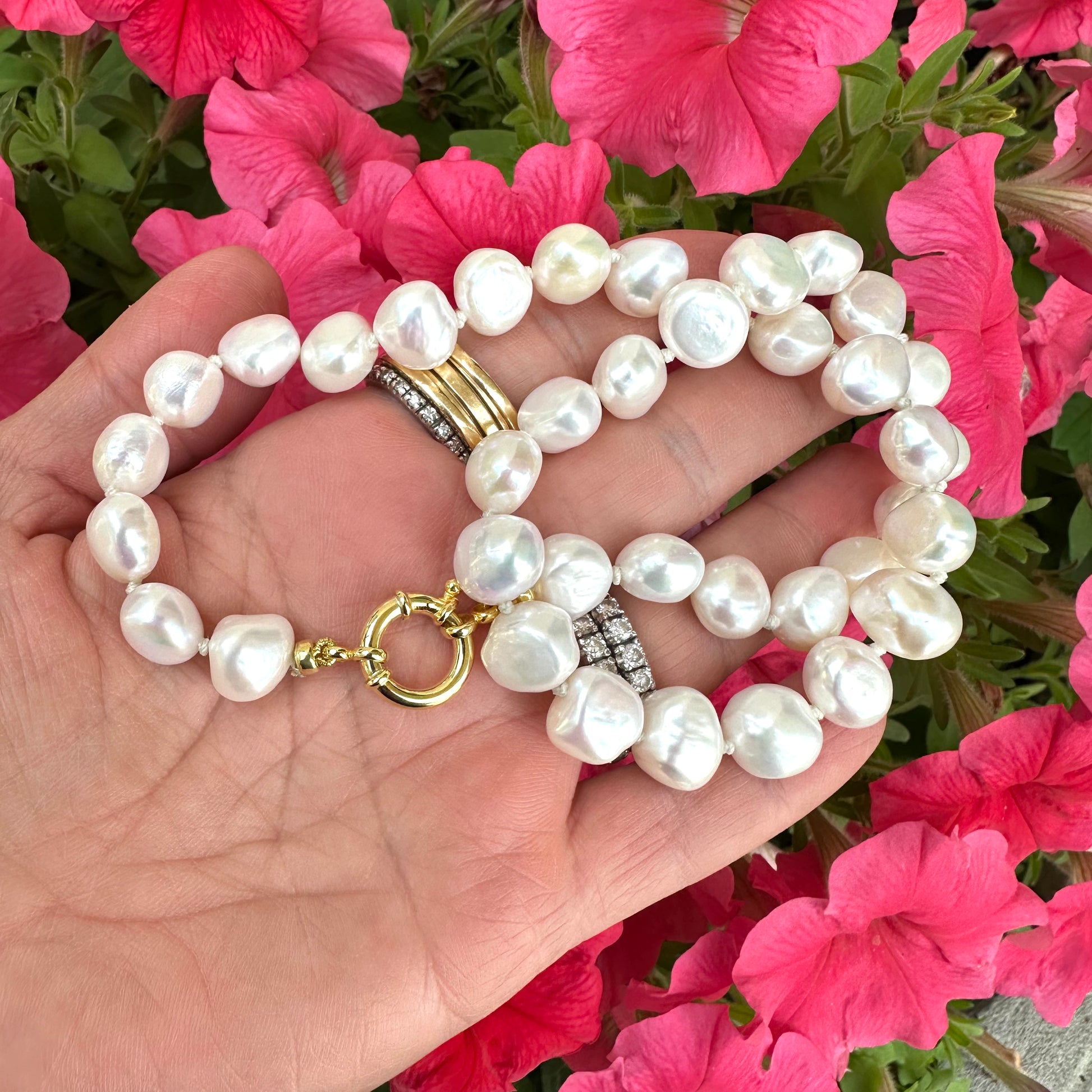 Small baroque pearl classic necklace displayed on a hand, surrounded by colorful pink flowers.