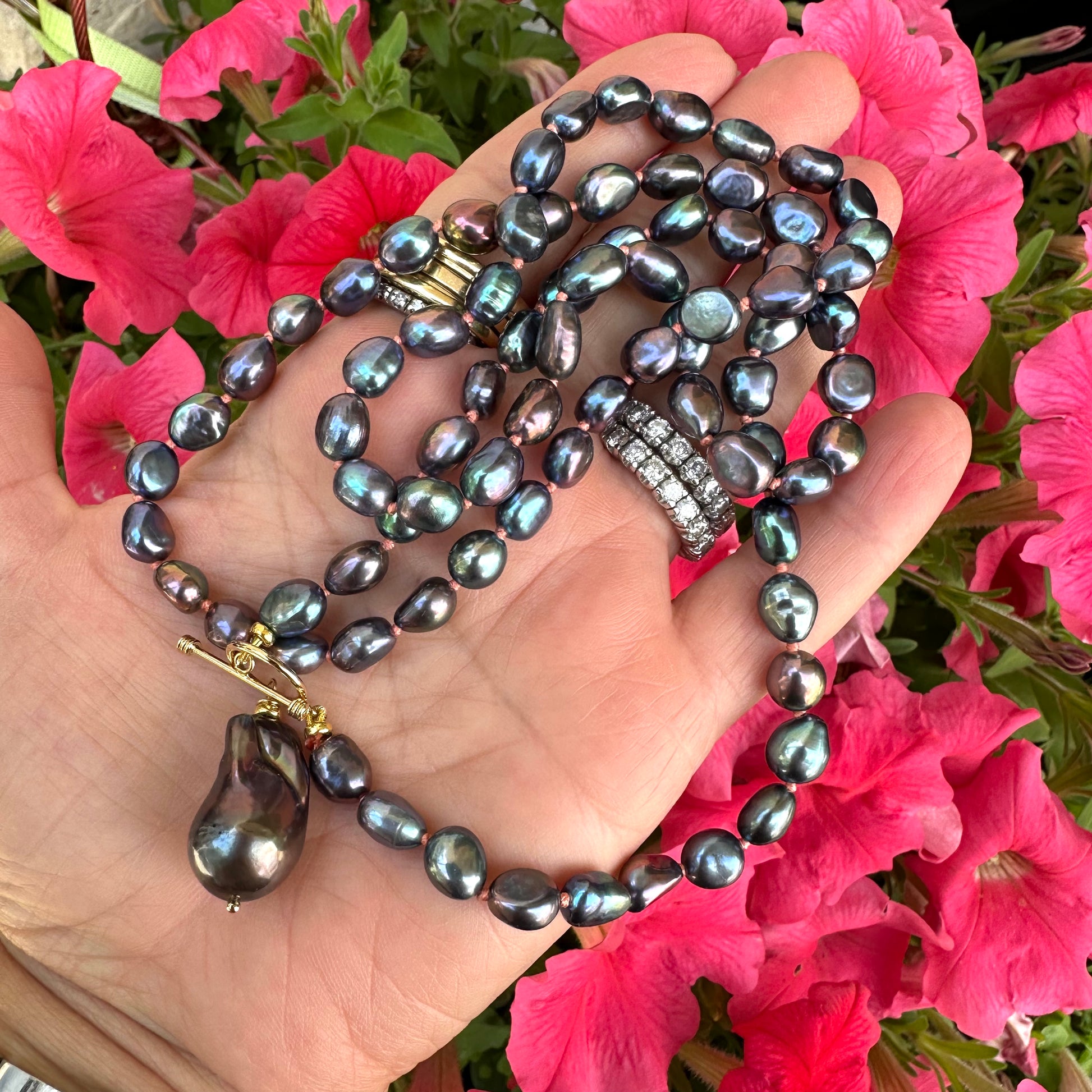Close-up of peacock black pearl necklace with baroque pendant held outdoors near foliage