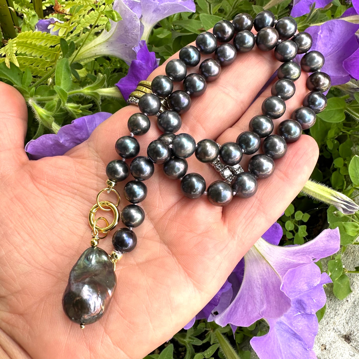 Close-up of black pearl necklace with removable pendant held in hand against floral background