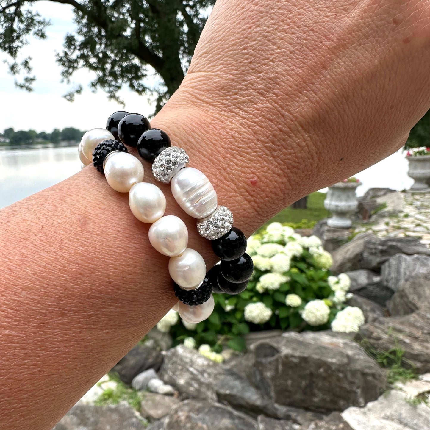 Two white pearl stretch bracelets with black rhinestones worn on woman's wrist in summer foliage