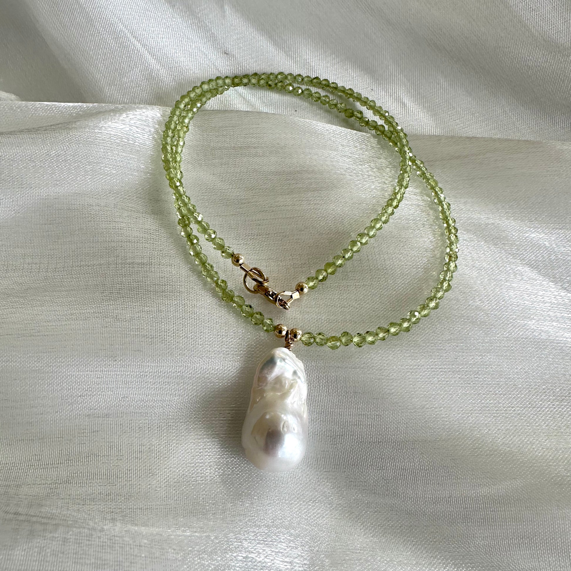 Peridot beaded necklace with baroque pearl pendant displayed on white cloth