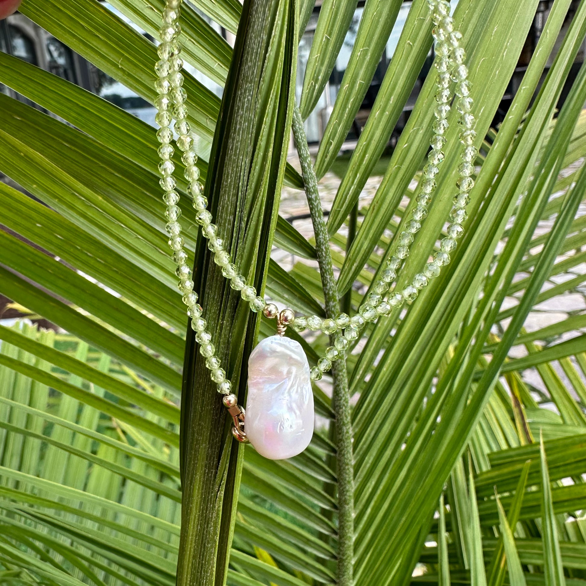 Peridot beaded necklace with baroque pearl pendant photographed against green foliage