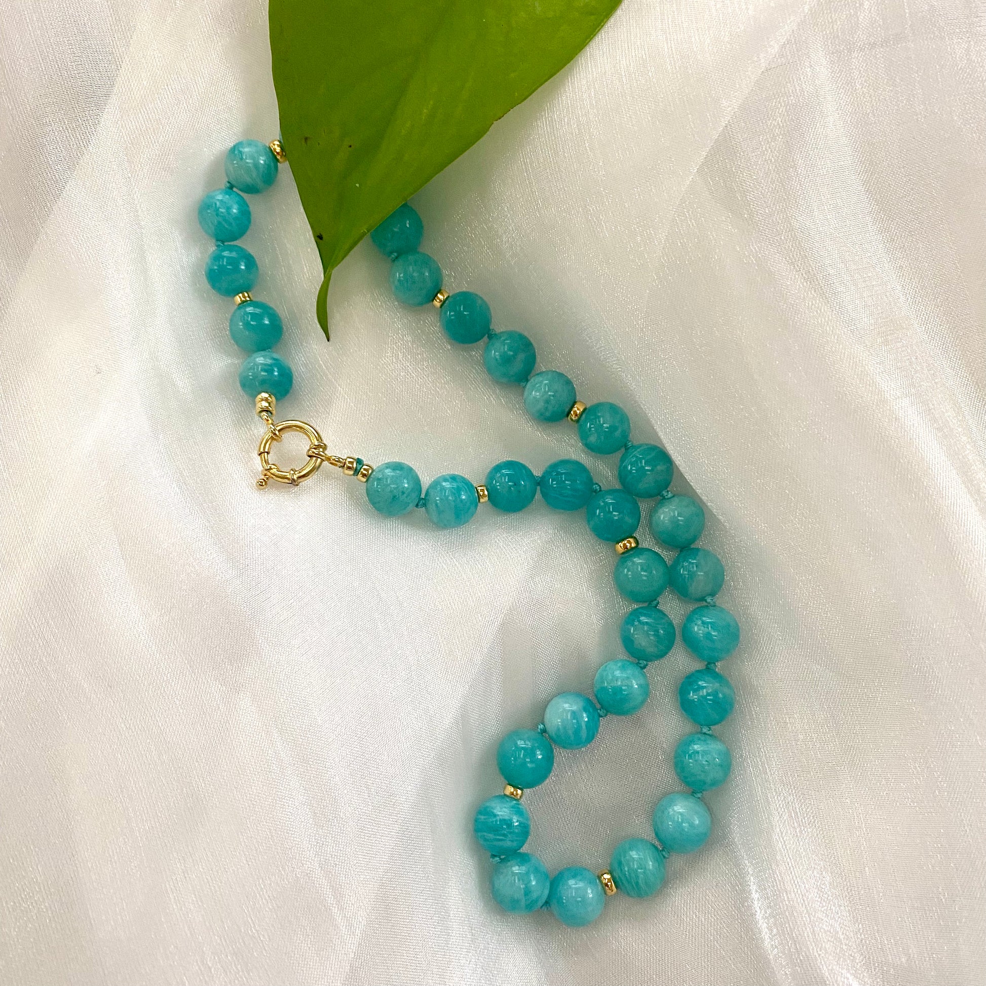 Blue Amazonite Beaded Necklace with gold accents resting on a soft white fabric.