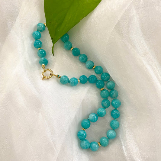 Blue Amazonite Beaded Necklace with gold accents resting on a soft white fabric.