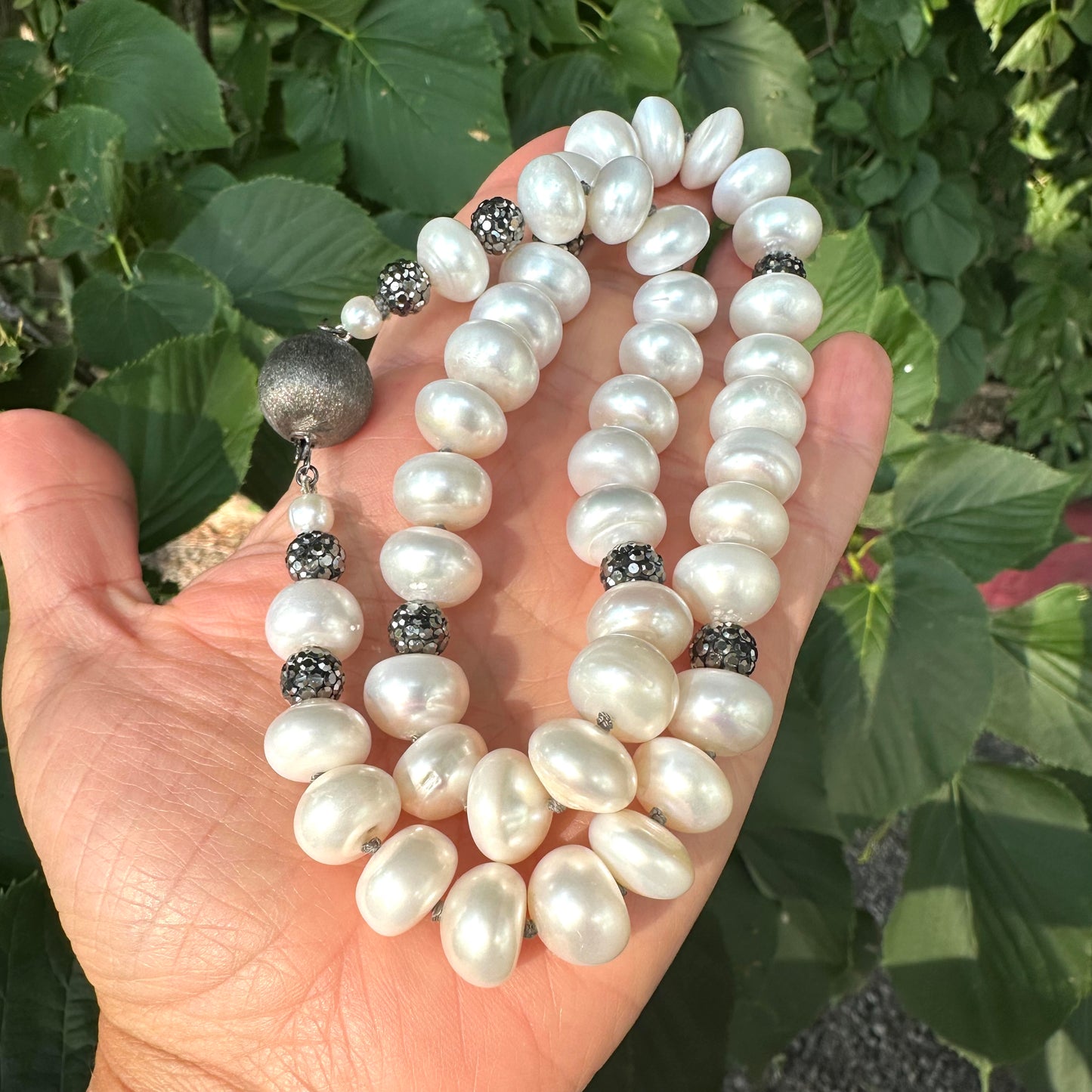 White button pearl necklace with rhinestone beads held in hand against green foliage
