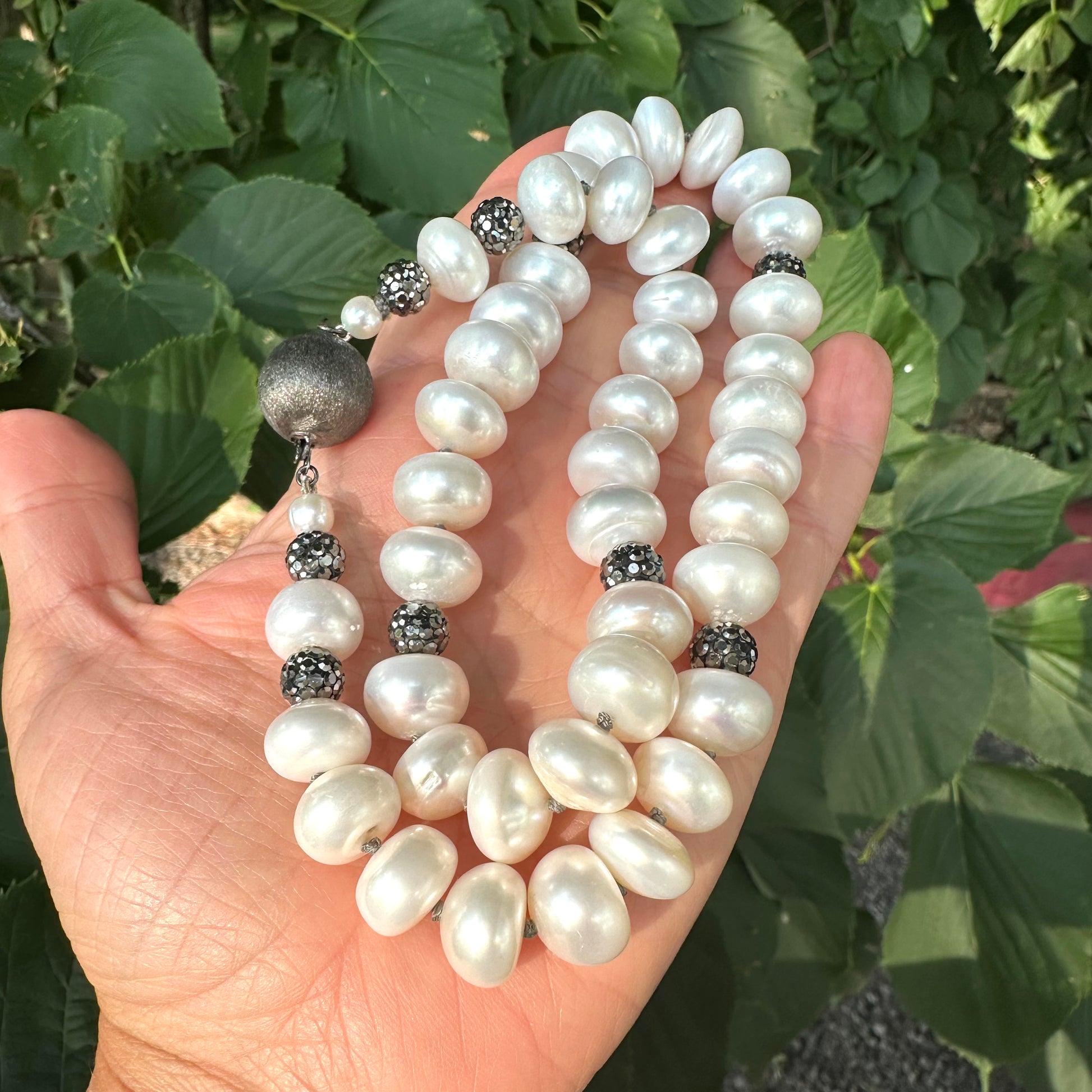 White button pearl necklace with rhinestone beads held in hand against green foliage