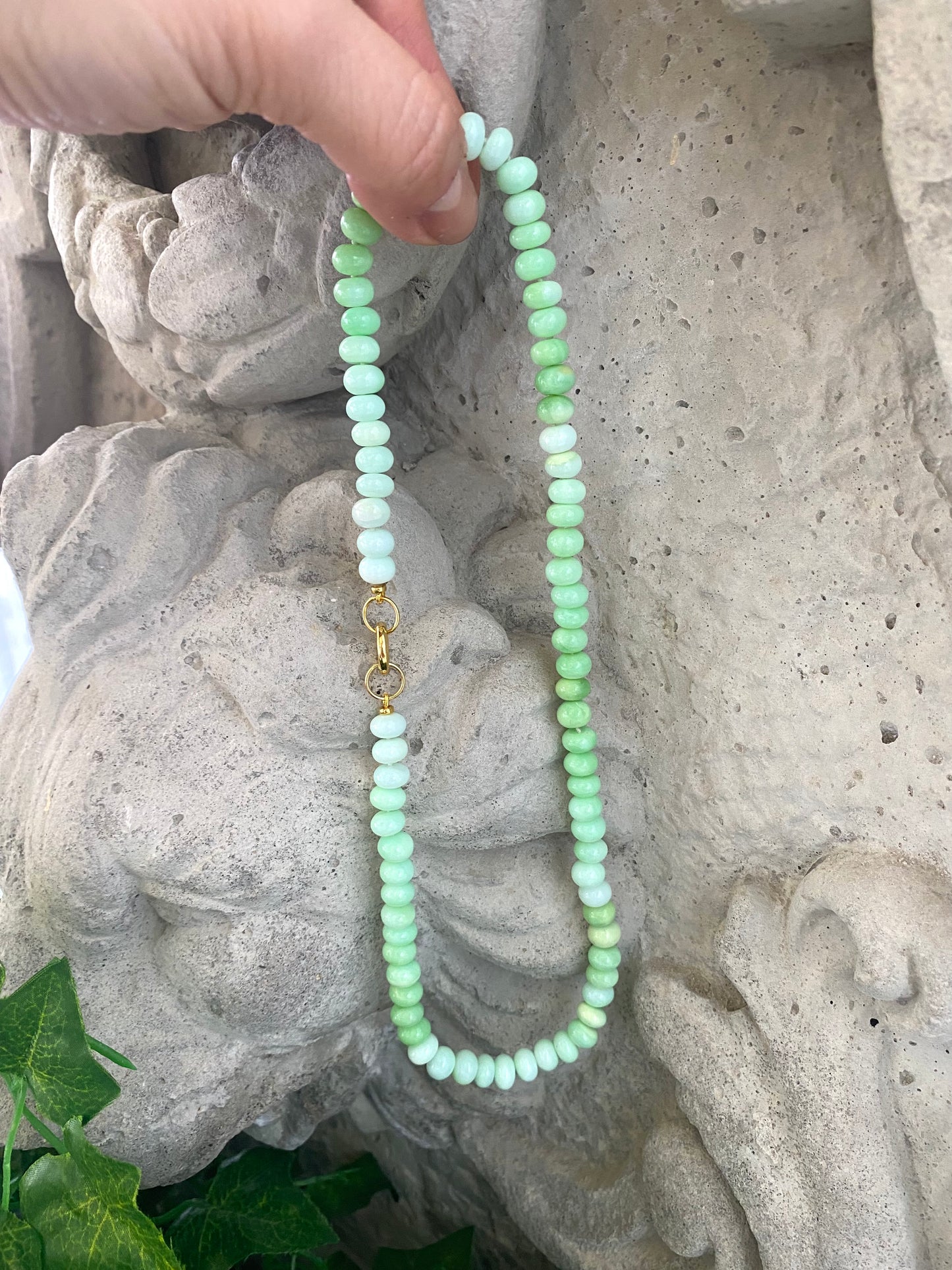Green opal beaded necklace held against stone statue background