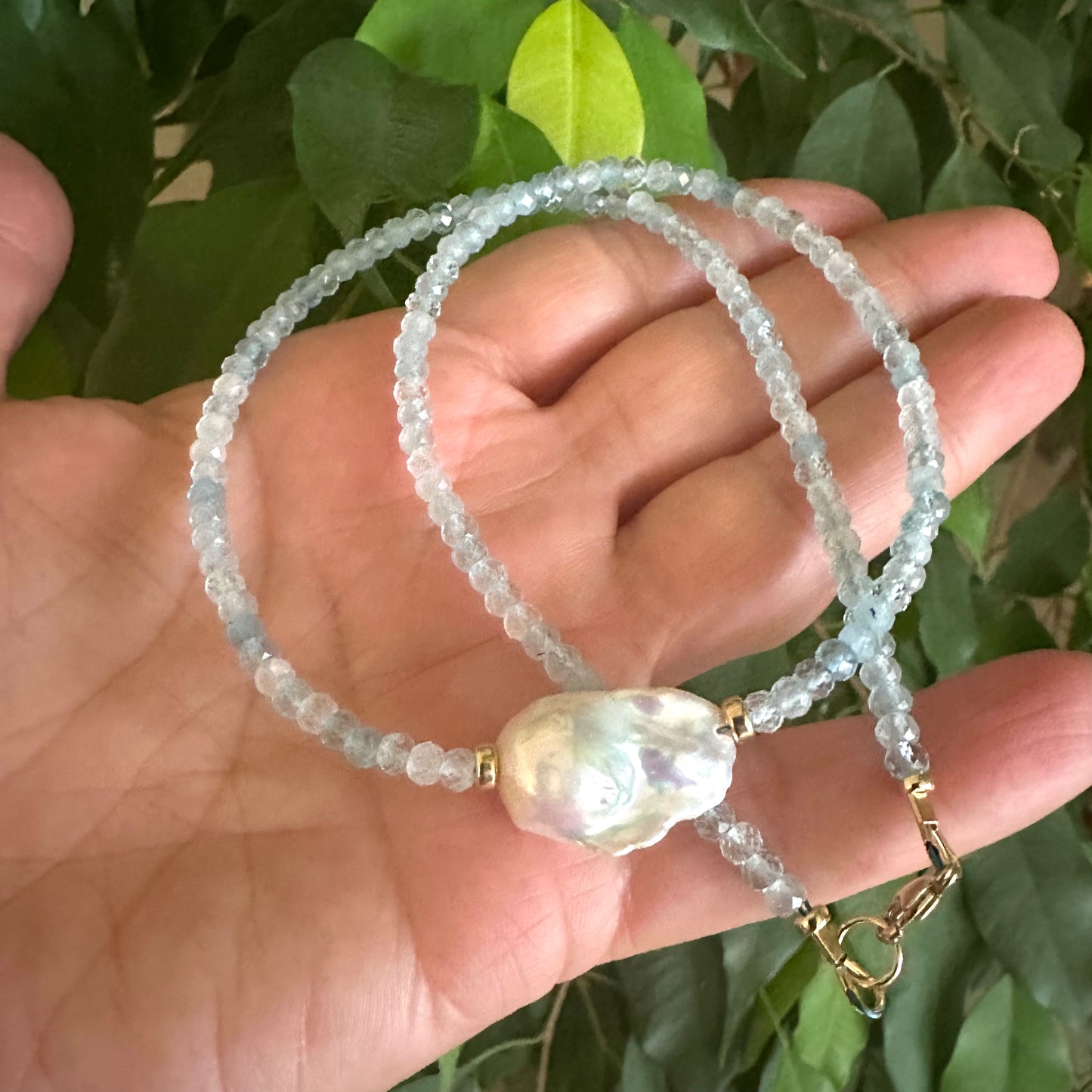Aquamarine pearl necklace close-up in hand with natural foliage