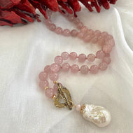 Rose quartz pearl necklace laid flat on white cloth, close-up detail