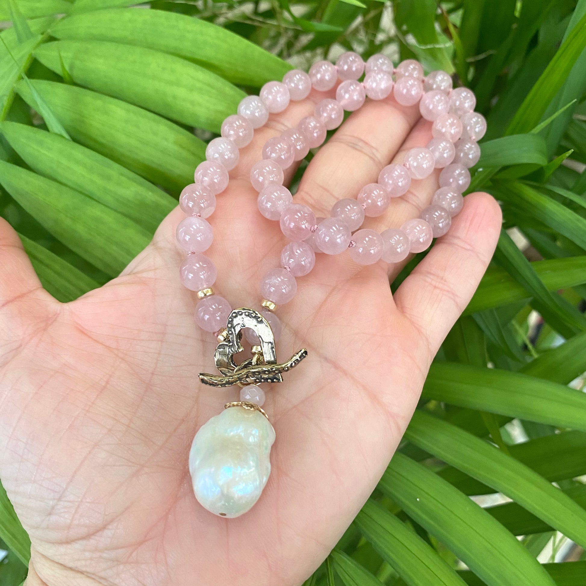 Rose quartz pearl necklace held in hand against green leaves