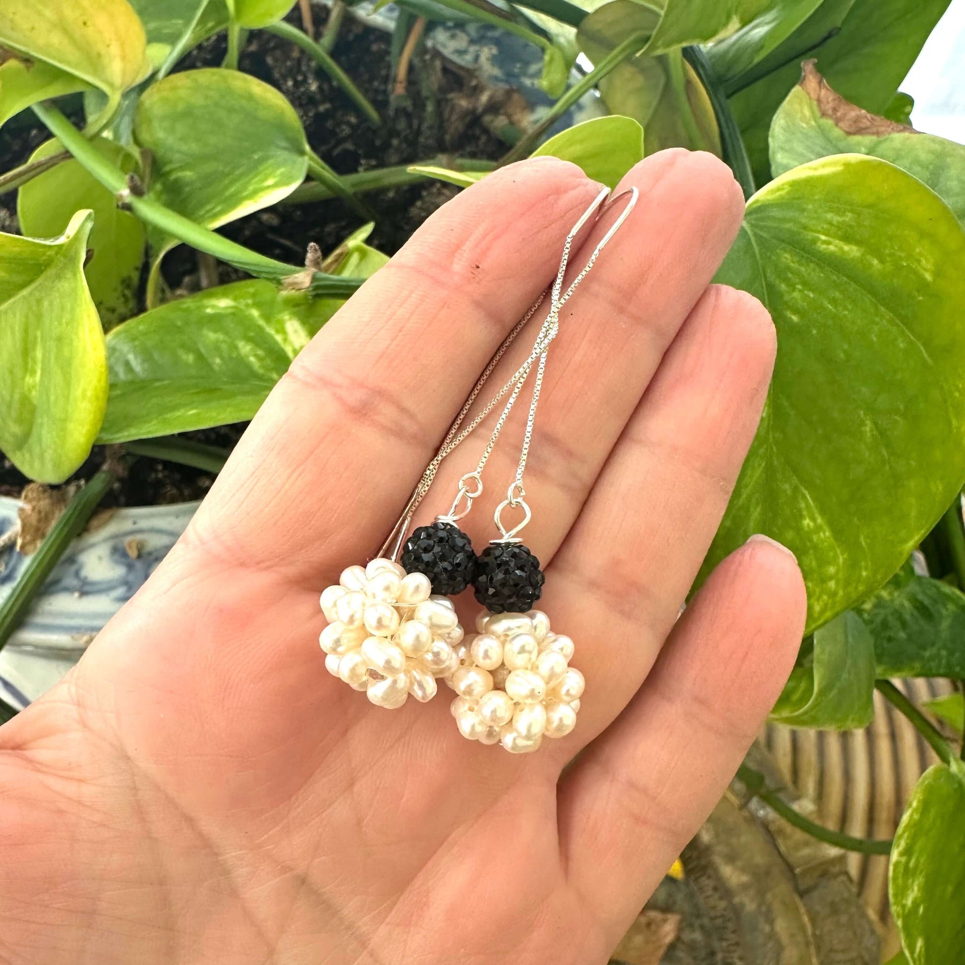 Hand holding white pearl threader earrings with black rhinestone pavé detail in natural outdoor light