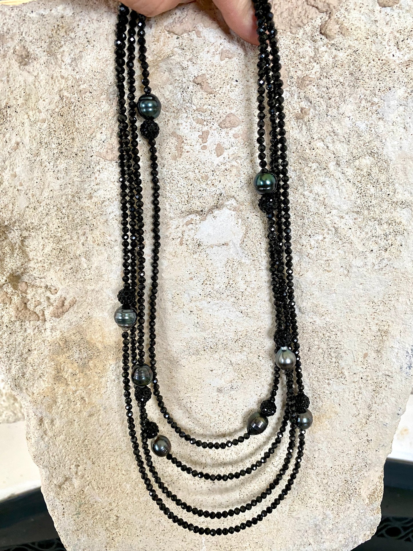 Black spinel pearl necklace laid on stone surface, detail view