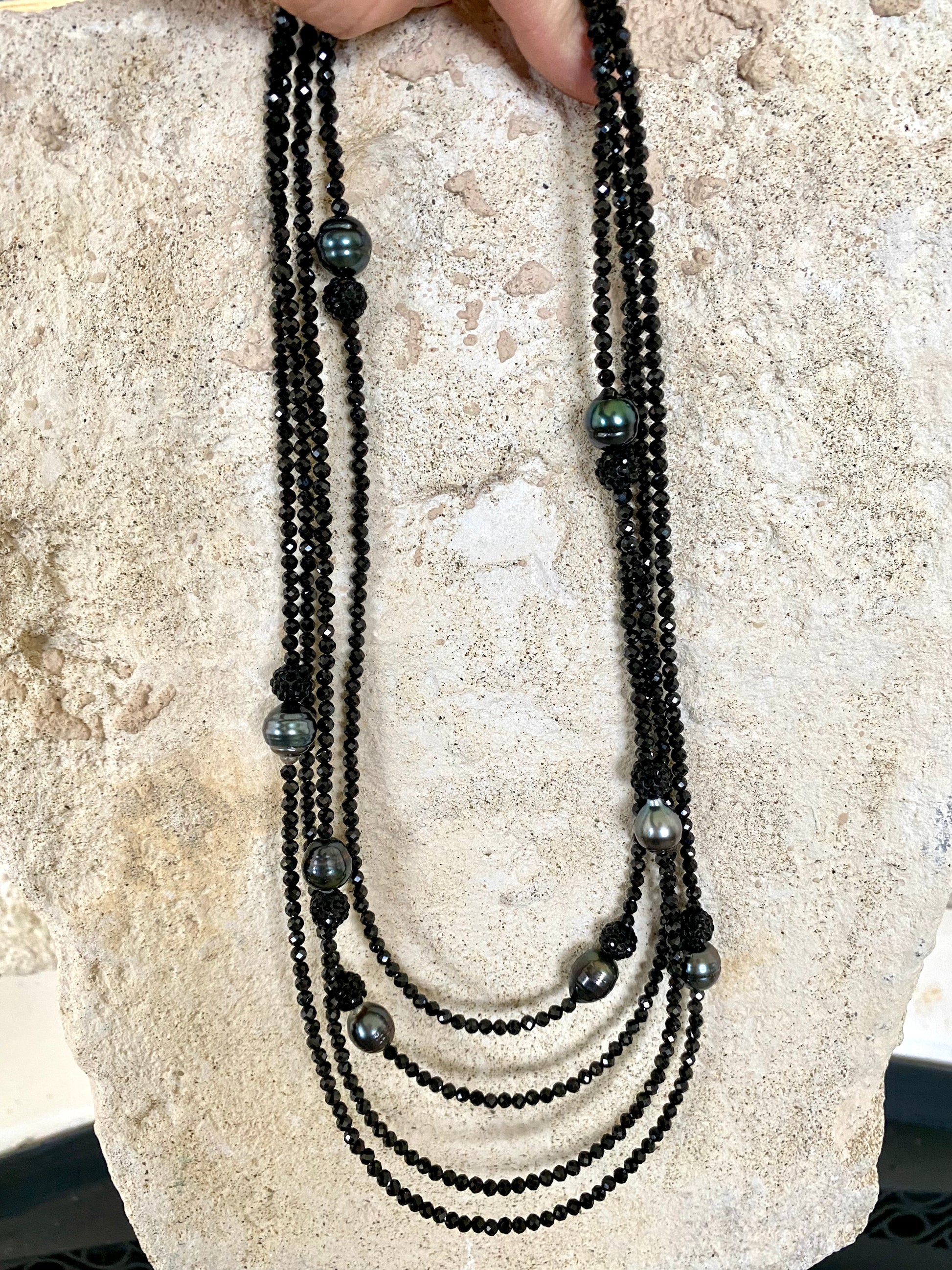 Black spinel pearl necklace laid on stone surface, detail view