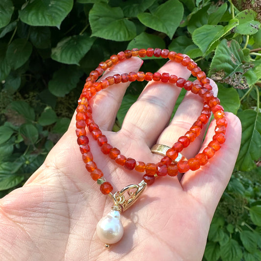 Carnelian toggle necklace with baroque pearl held in hand showing faceted carnelian beads
