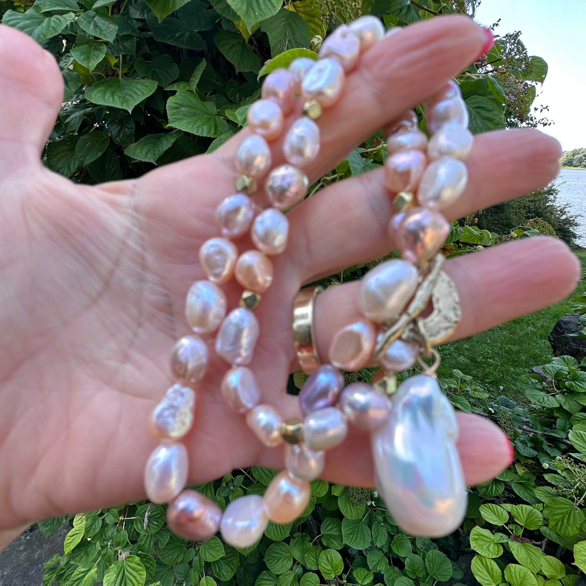 Close-up of pastel pearl necklace showing white, pink, and peach pearls held near foliage
