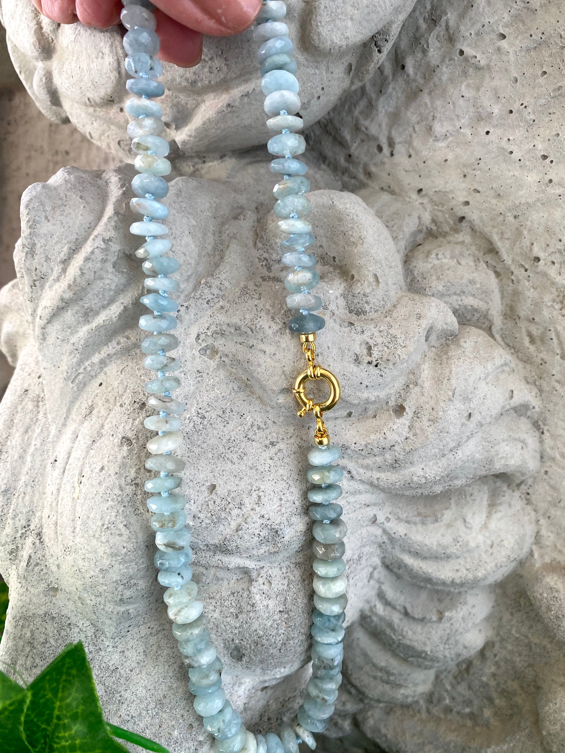 Aquamarine beaded necklace held against natural outdoor stone