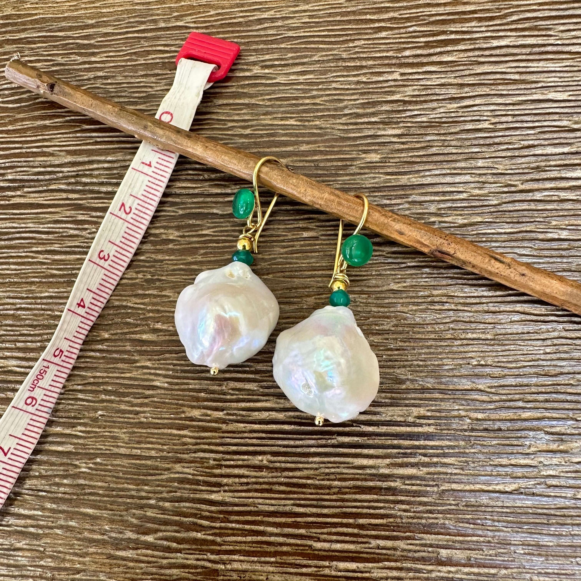 White baroque pearl drop earrings with green agate and gold accents on a wooden background