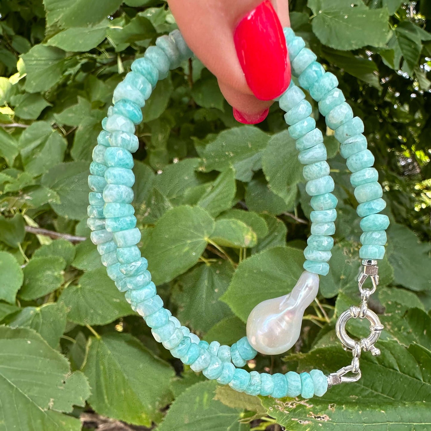 Amazonite and white baroque pearl necklace displayed outdoors against green leaves background
