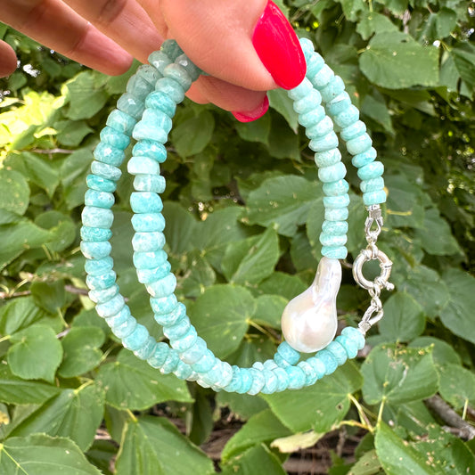 Amazonite and white baroque pearl necklace held in hand against green foliage, natural light view