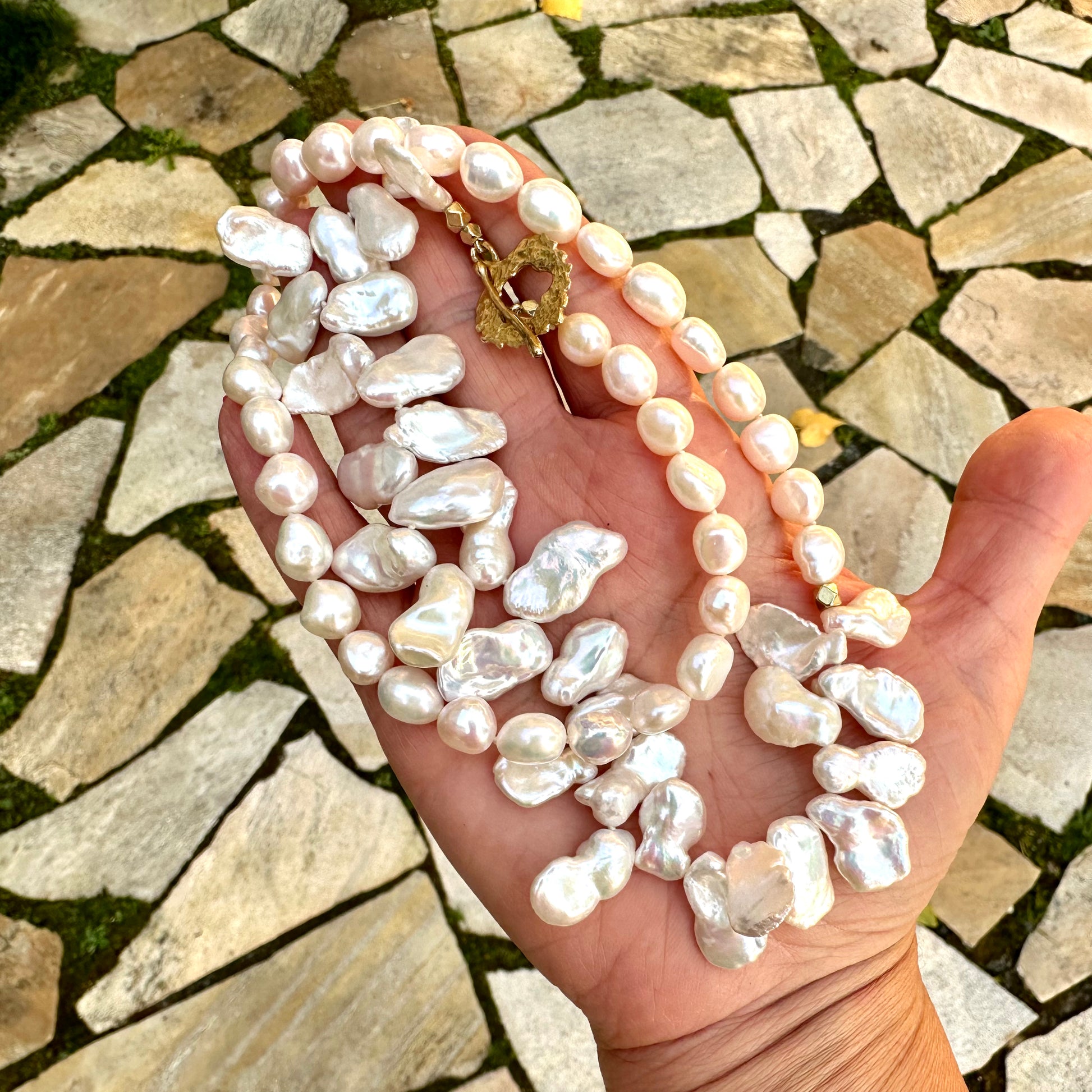 White keshi pearl necklace held in hand against garden tile backdrop in natural light