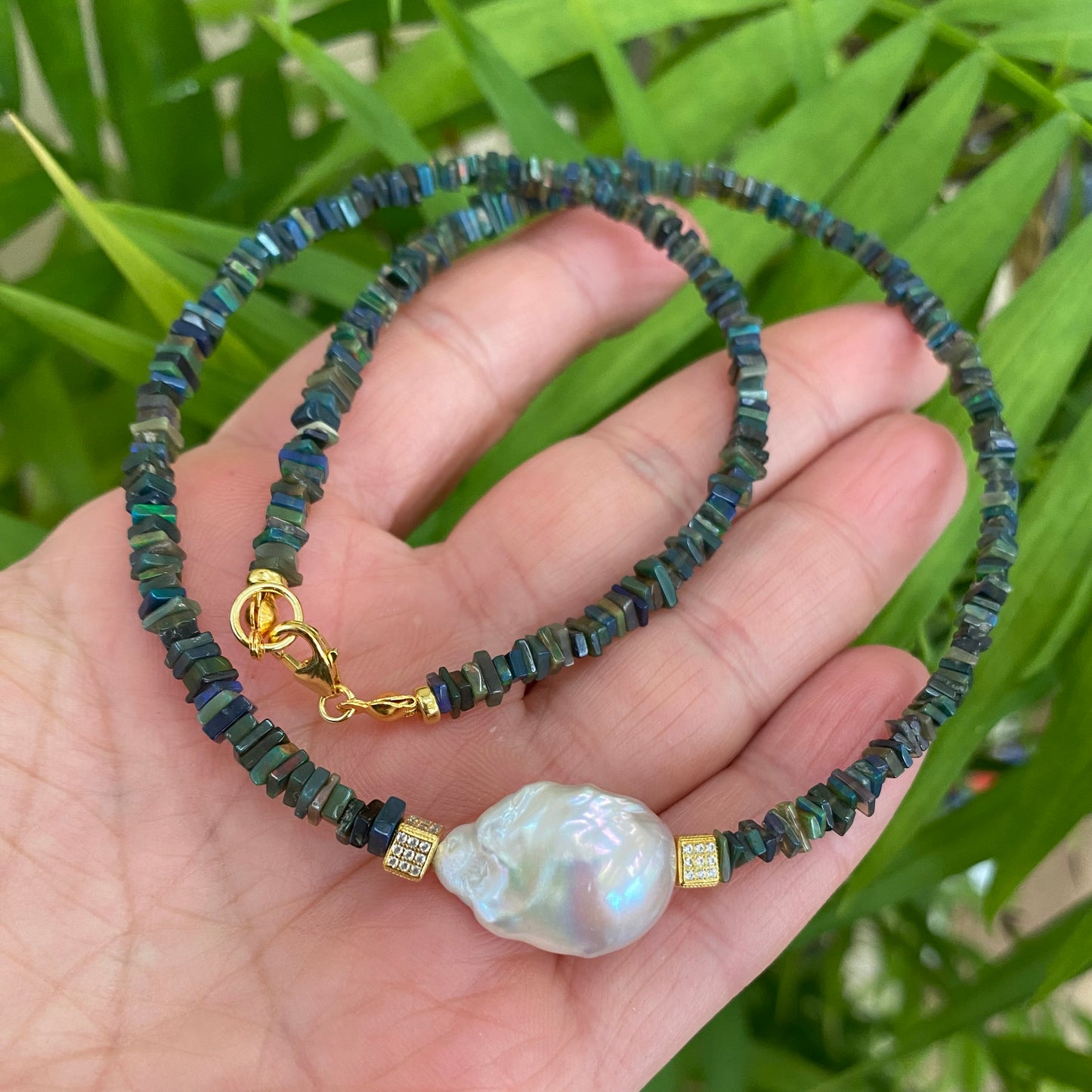 Black opal pearl necklace in hand with natural stone colors visible