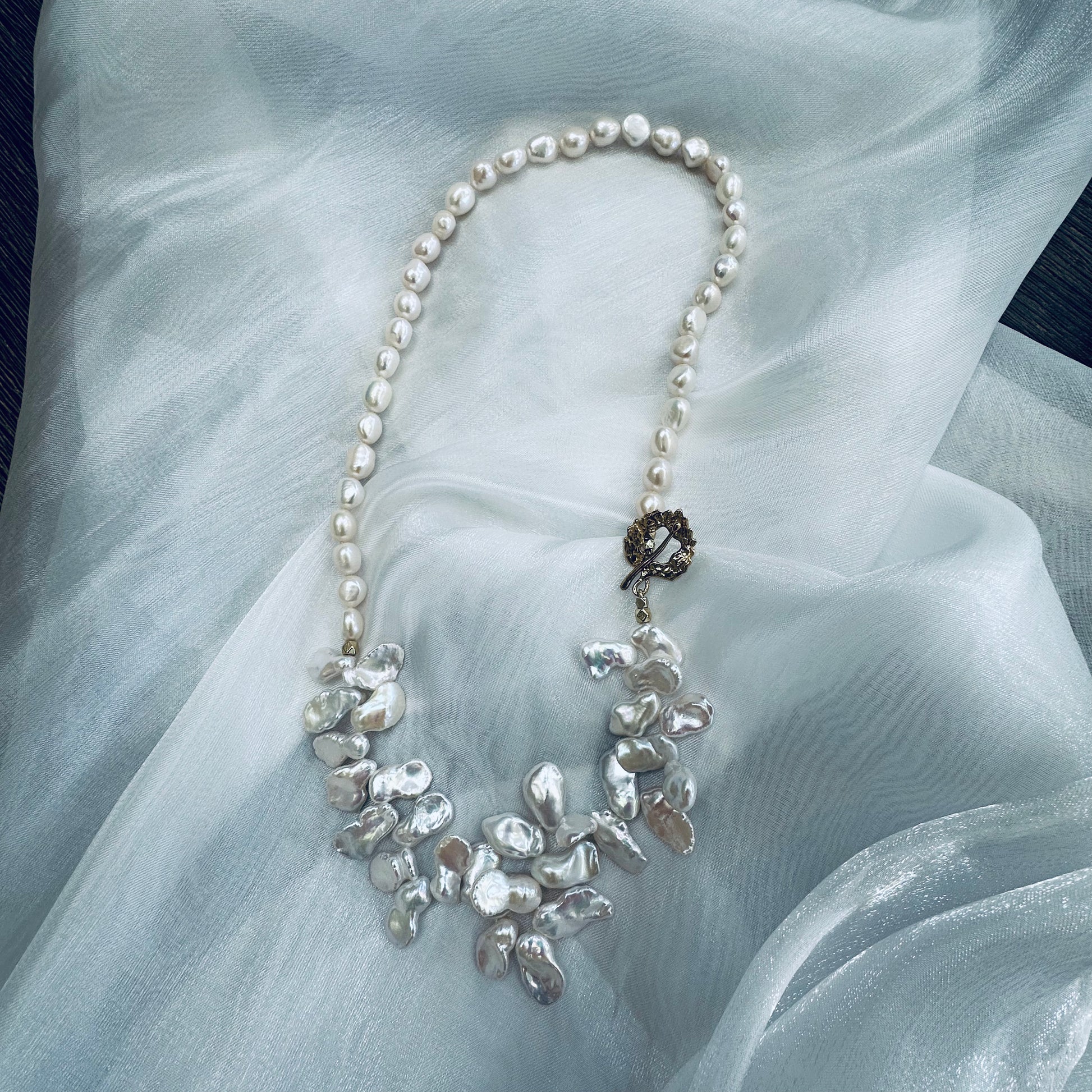 White keshi pearl necklace displayed on white cloth table showing nugget and petal pearls