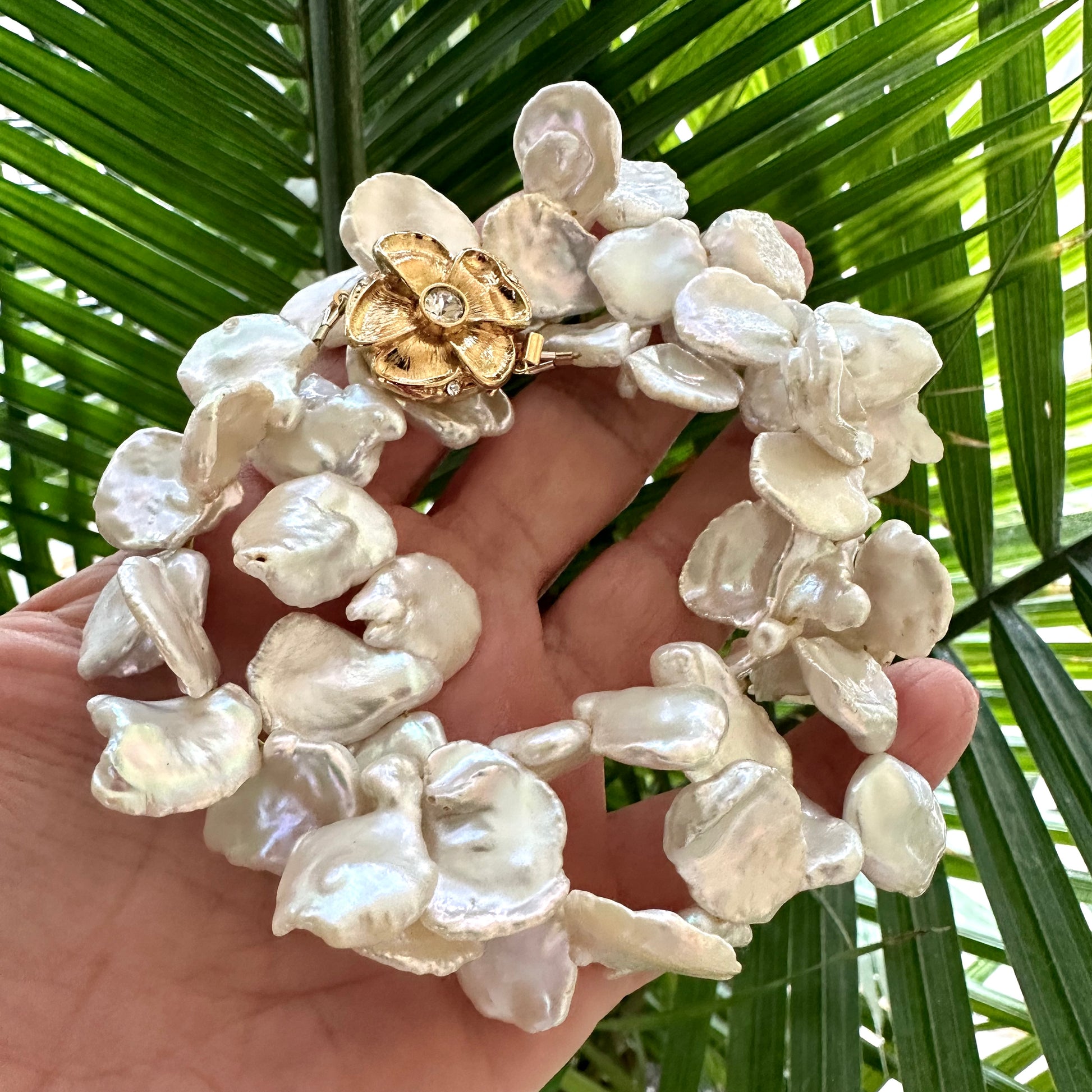 White keshi pearl necklace with flower clasp held in hand against green foliage background