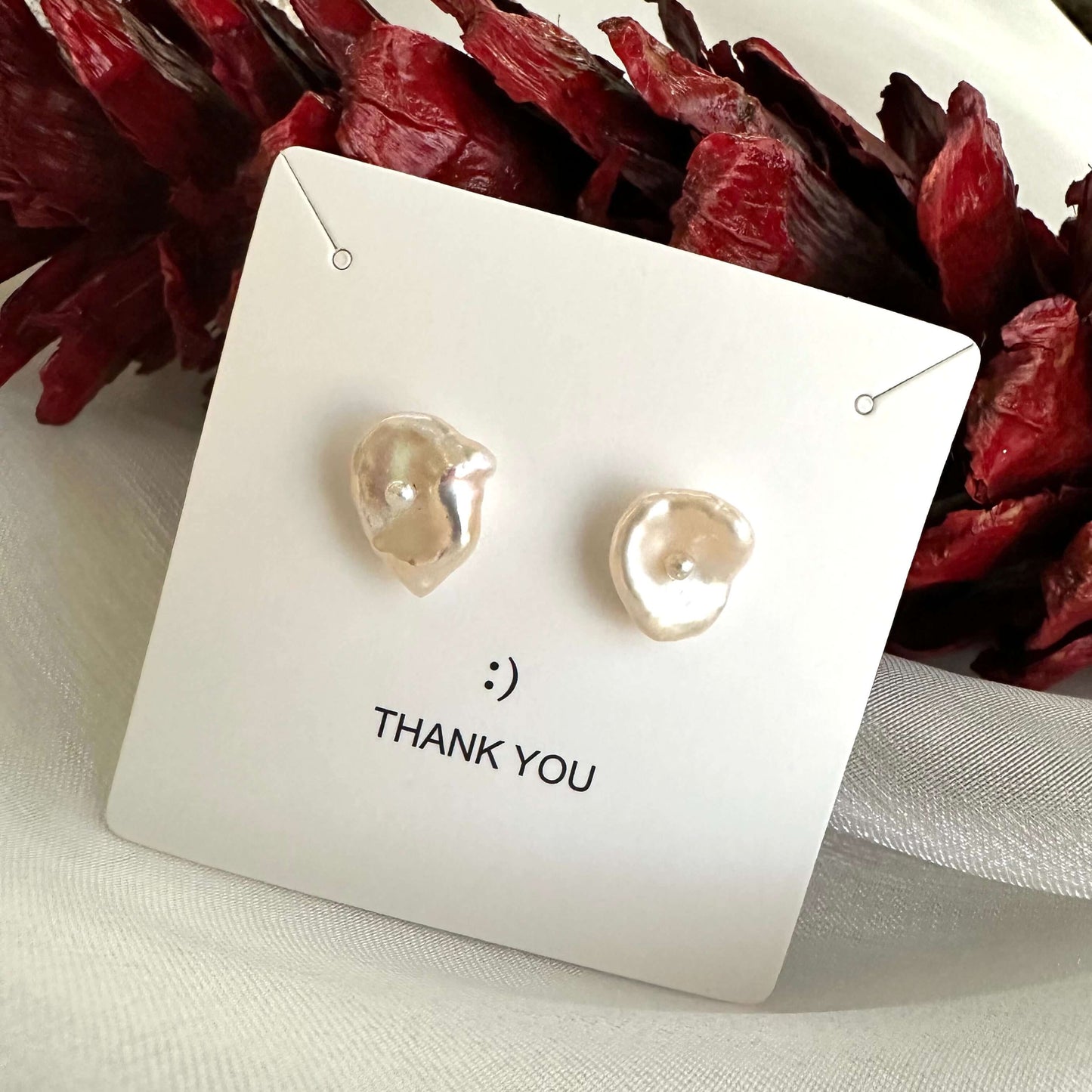 White flower pearl stud earrings in gift box beside red pine cone, showing festive packaging and romantic handmade design.