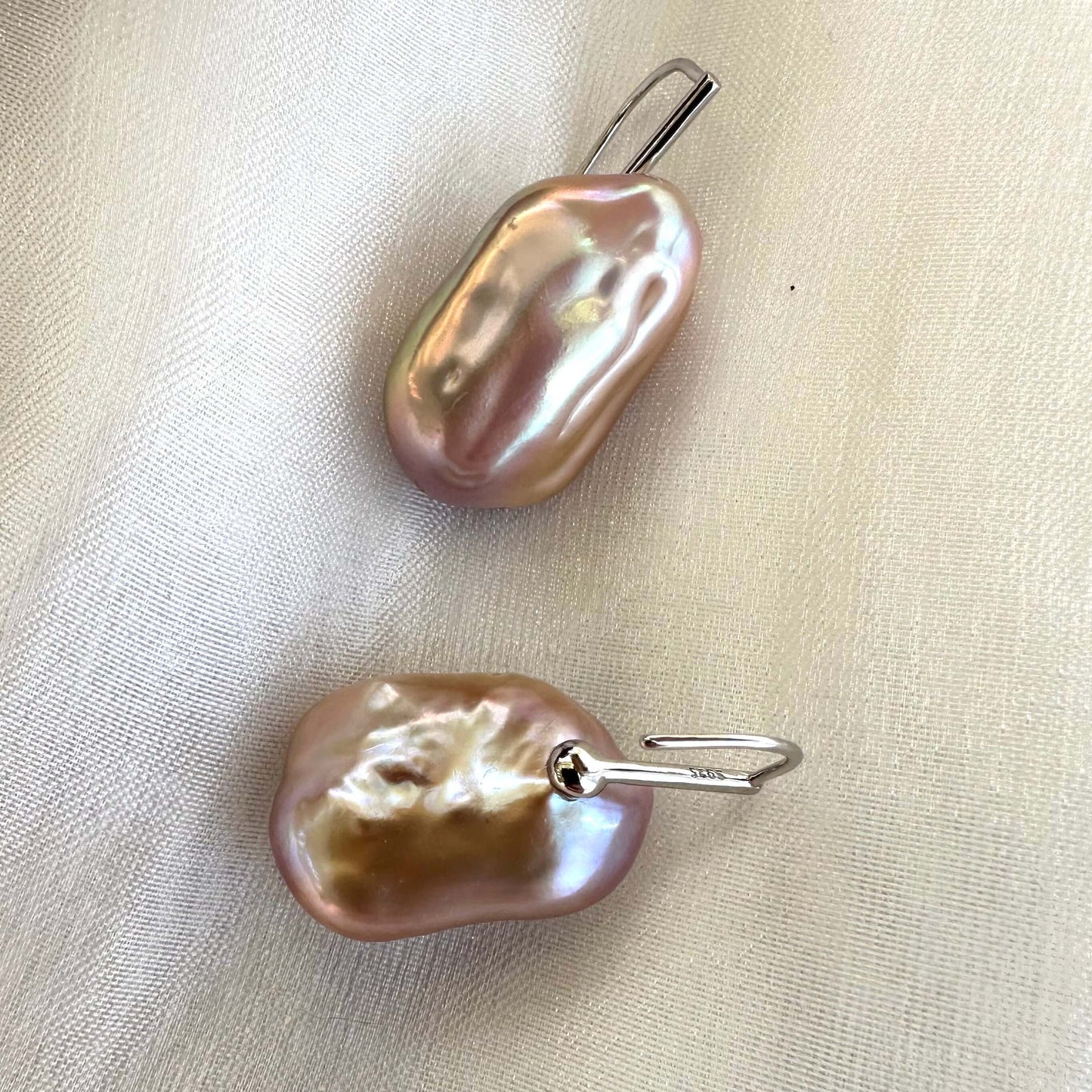Purple pearl drop earrings with large baroque pearls on shell, capturing organic detail and radiant pinkish-lavender sheen.