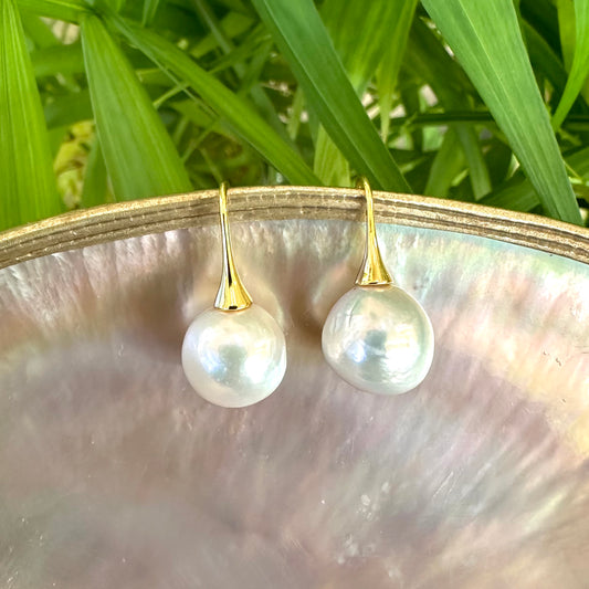 White pearl drop earrings with gold vermeil hooks displayed on pearl shell and green leaves, highlighting lustrous Edison pearls.