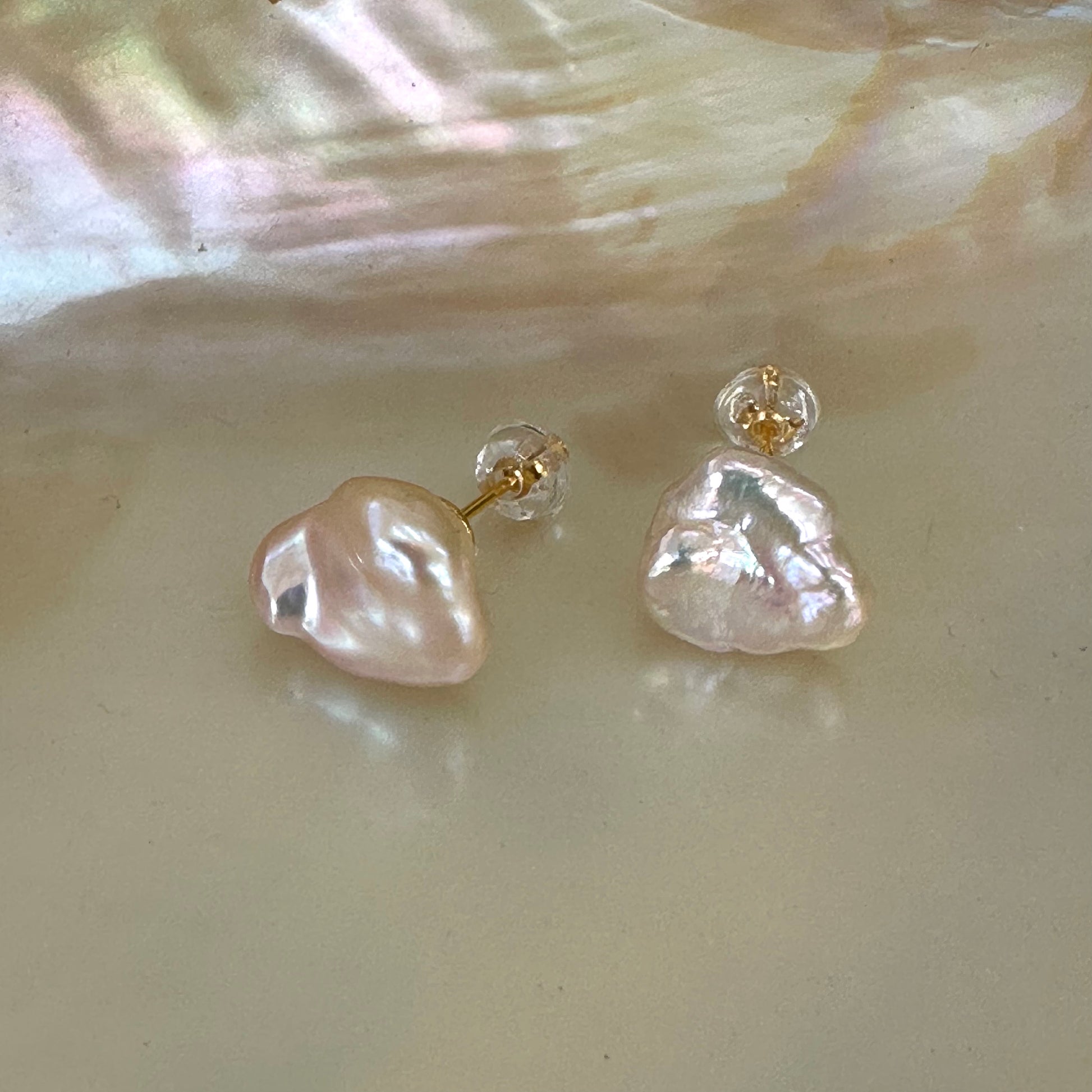 Champagne keshi pearl stud earrings in gold vermeil resting on white pearl shell, showing soft pink-golden luster and petal shape.