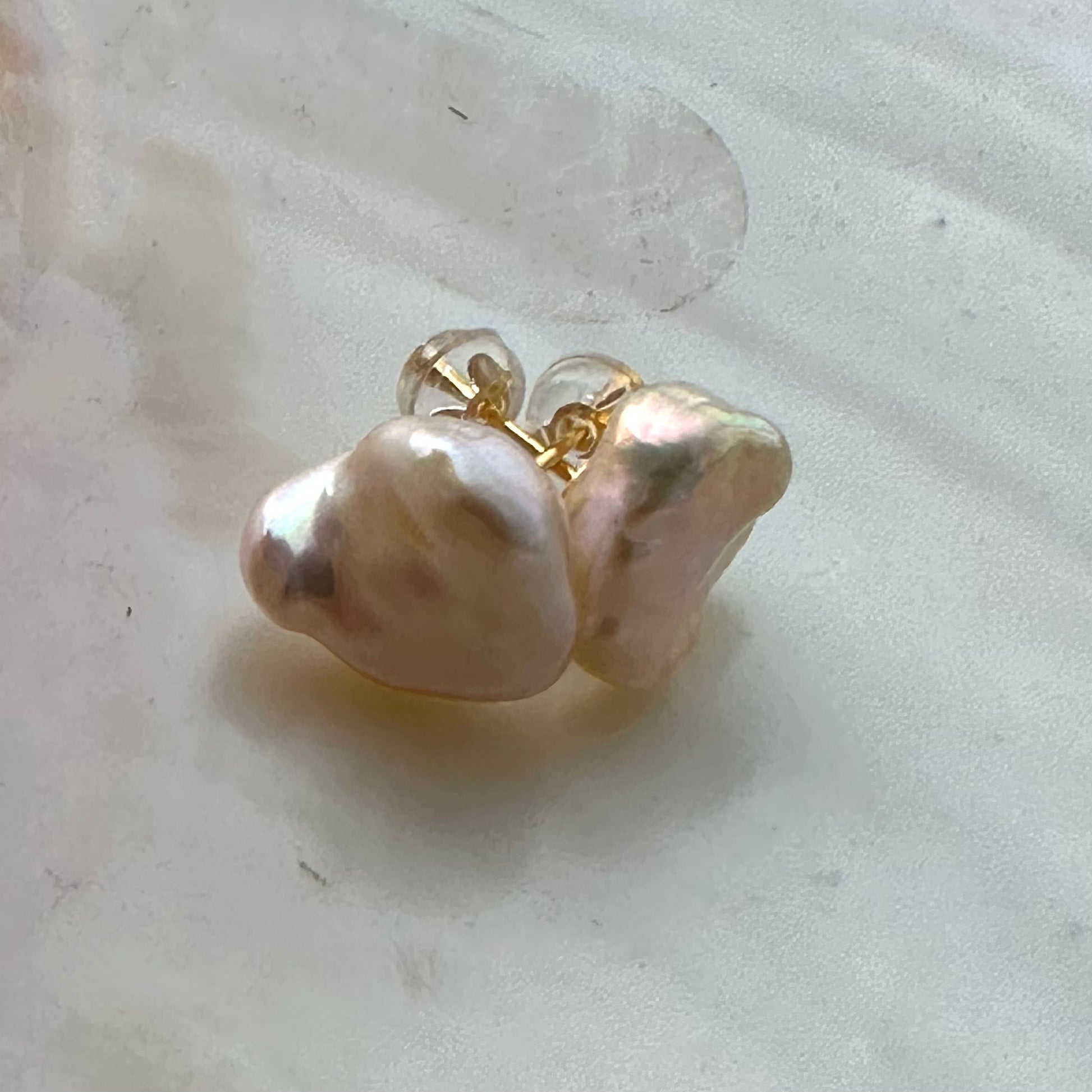 Champagne keshi pearl stud earrings on white shell, capturing luminous tone, handcrafted design, and delicate texture of pearls.